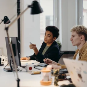 Two people sitting at a table with computers.