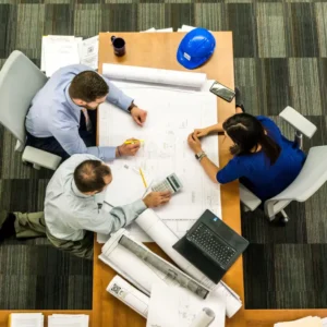 Three people sitting at a table with papers and pens.